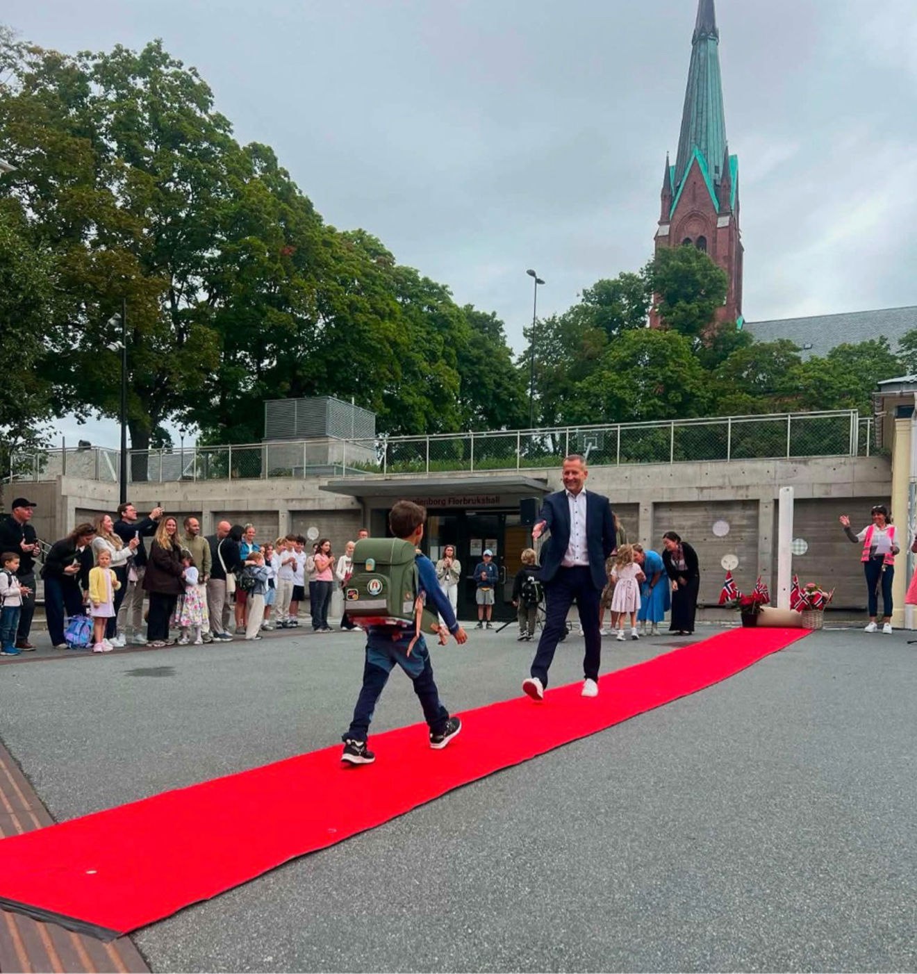 en gruppe mennesker som går på en rød sti med en høy bygning i bakgrunnen