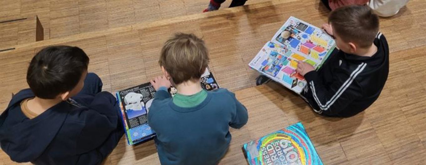 En gruppe barner som sitter på gulvet og ser på en bok En gruppe barner som sitter på gulvet og ser på en bok